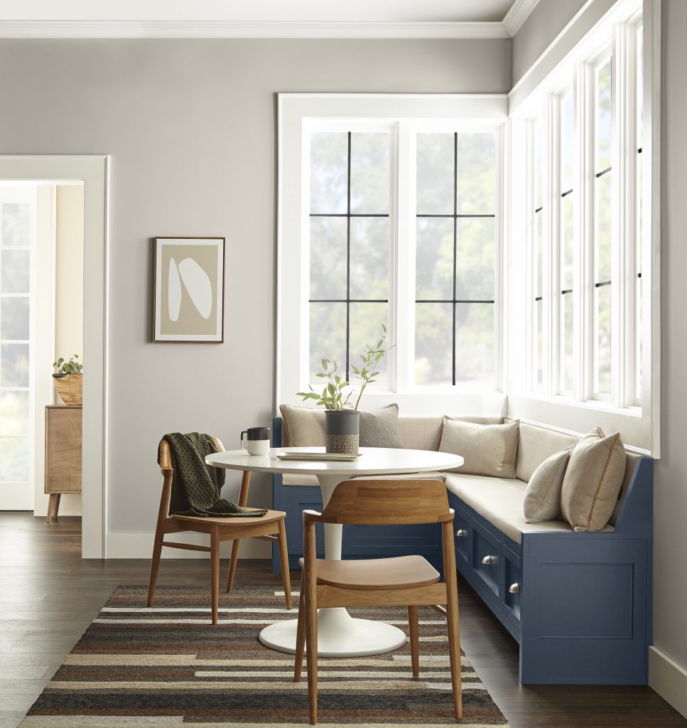 A farmhouse style breakfast nook with large windows, neutral wall and a dark blue wooden bench. 