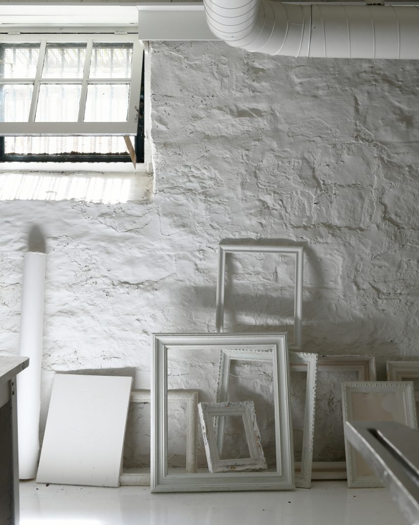 A white brick wall with white painted picture frames leaning against it.