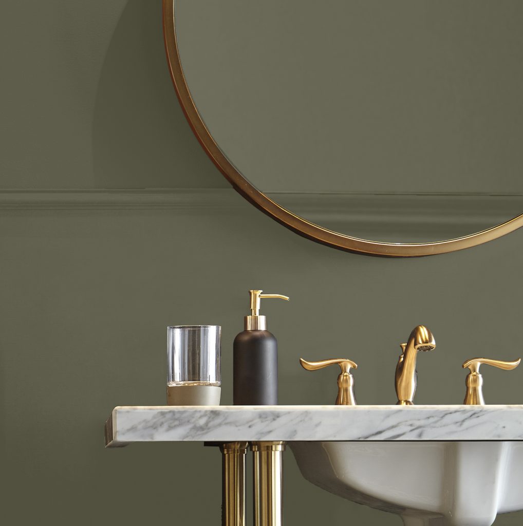 A bathroom detail image, the color on the wall is a deep, moody green called Mountain Olive.  The color of the mirror and hardware are a metallic gold. 