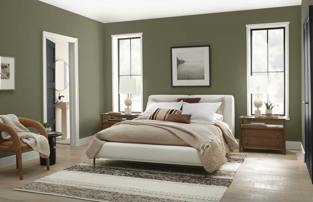 A master bedroom painted in a cozy deep olive green color.  The bedding and décor are a neutral color. 