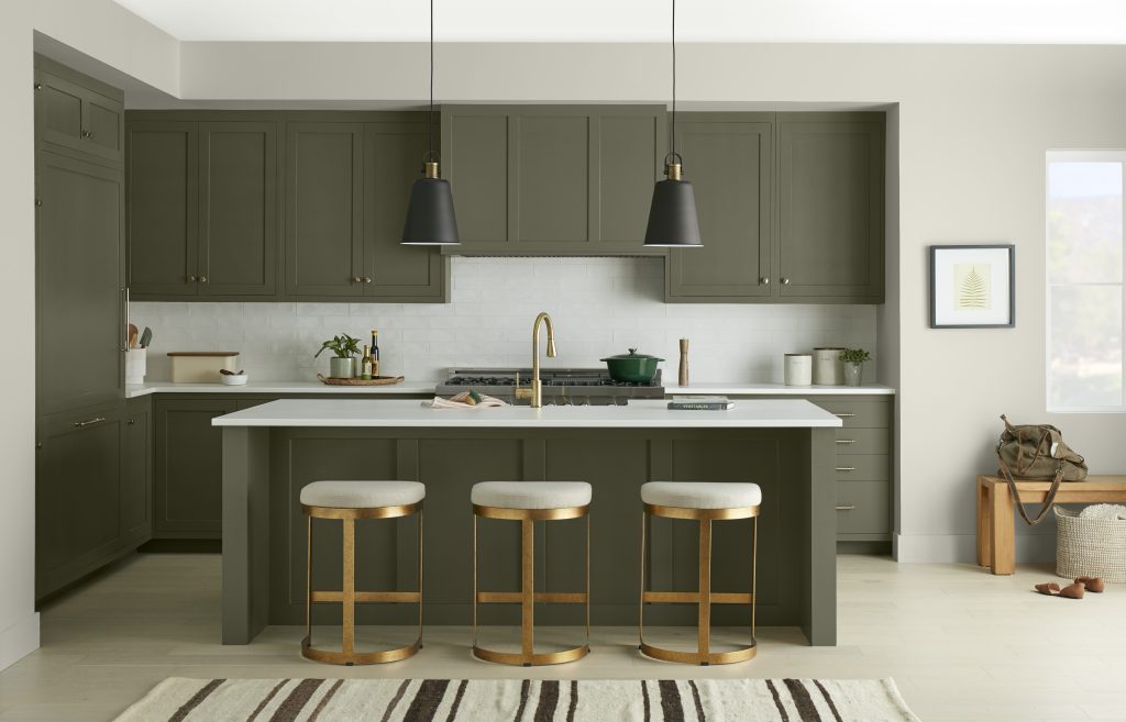 A modern kitchen with all green cabinetry.  The hardware and seating stool are metallic gold ideal for winter aesthetic. 