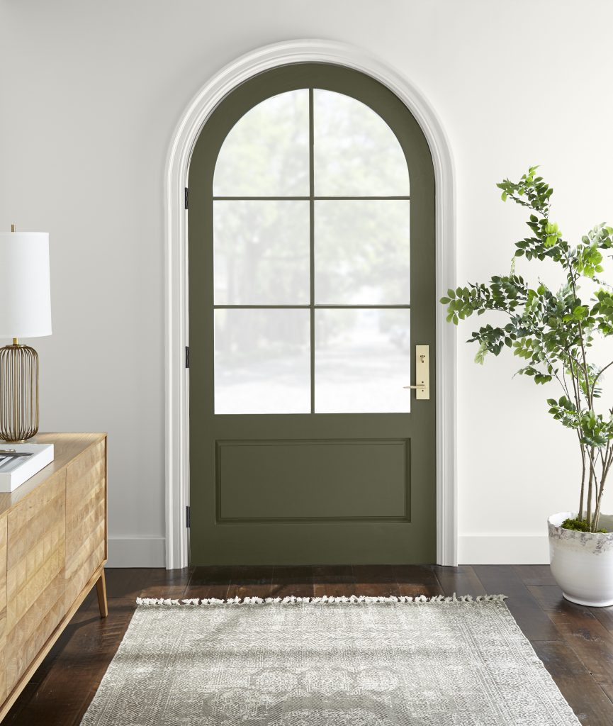 The image of an entryway with a green arched door. Walls and trim are a white color which provides contrast against the Olive Green door. 