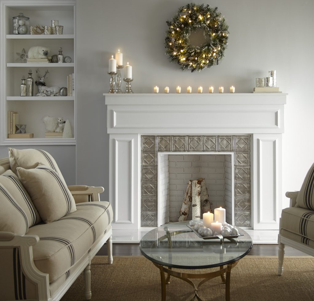 A living room with a fireplace and a lighted wreath on the wall and candles lit on the mantle.