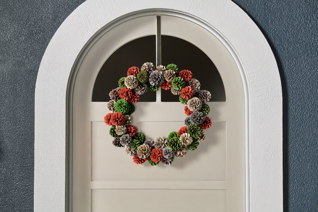Exterior white door with a spray painted pinecone wreath hanging on the door. 