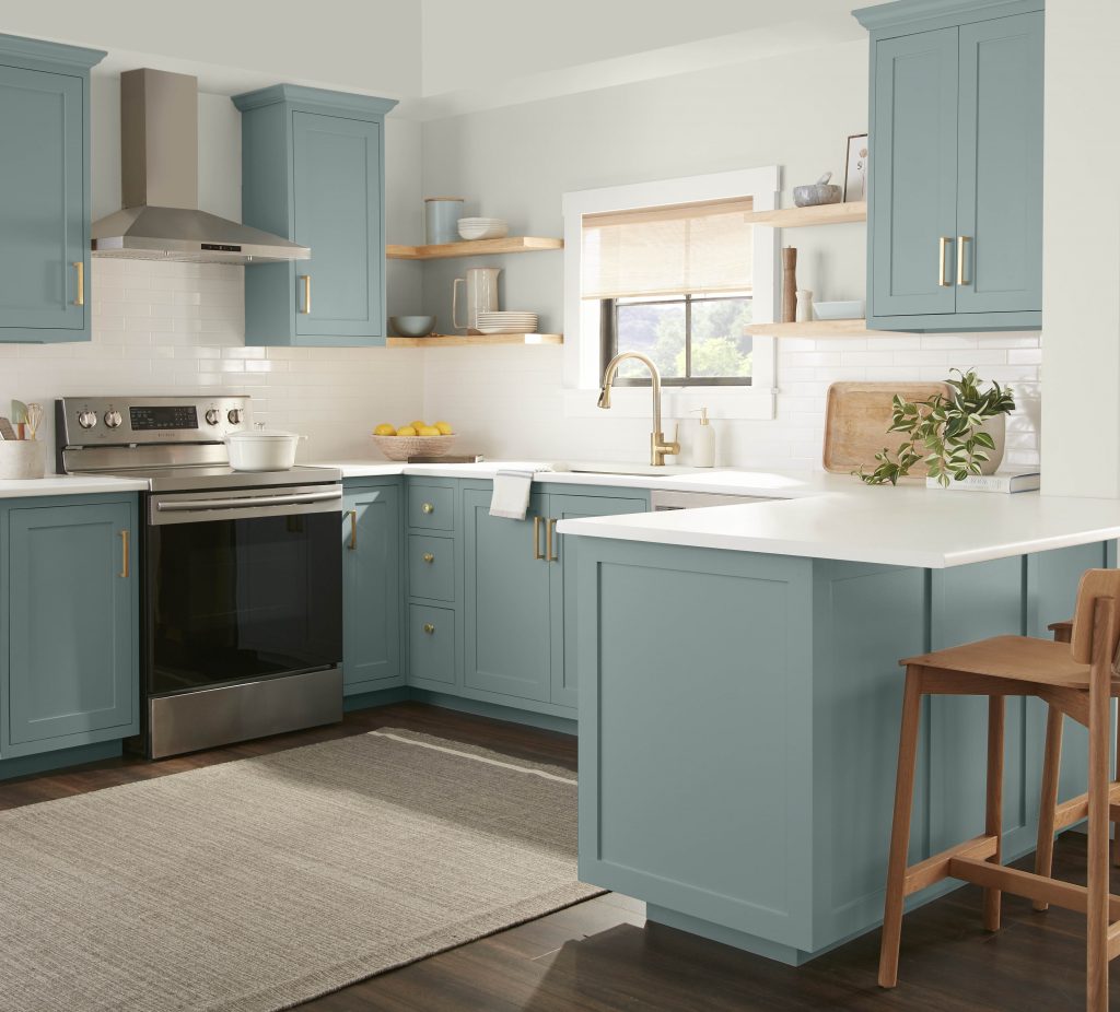 A casual kitchen with blue cabinetry and gold tones metallic hardware. There are four free standing open shelves in a warm wood tone. 