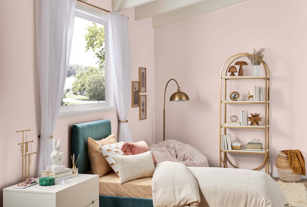 A teen bedroom with a cottage-core aesthetic.  The walls are pink and the décor accents are metallic gold. 