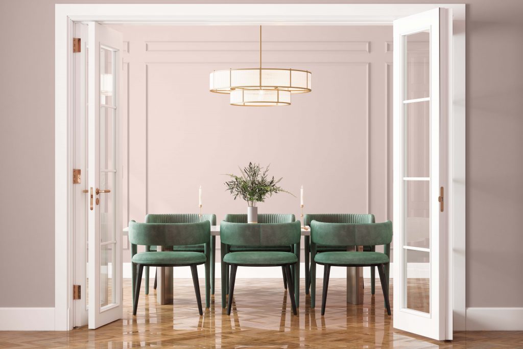 The entrance of a dining room with dining table, green velvet chairs and pink wall in background