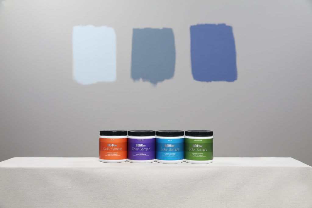 Image of three painted swatches on the wall of three different colors. In the foreground is a row of BEHR Color Sampes in different sheens. 