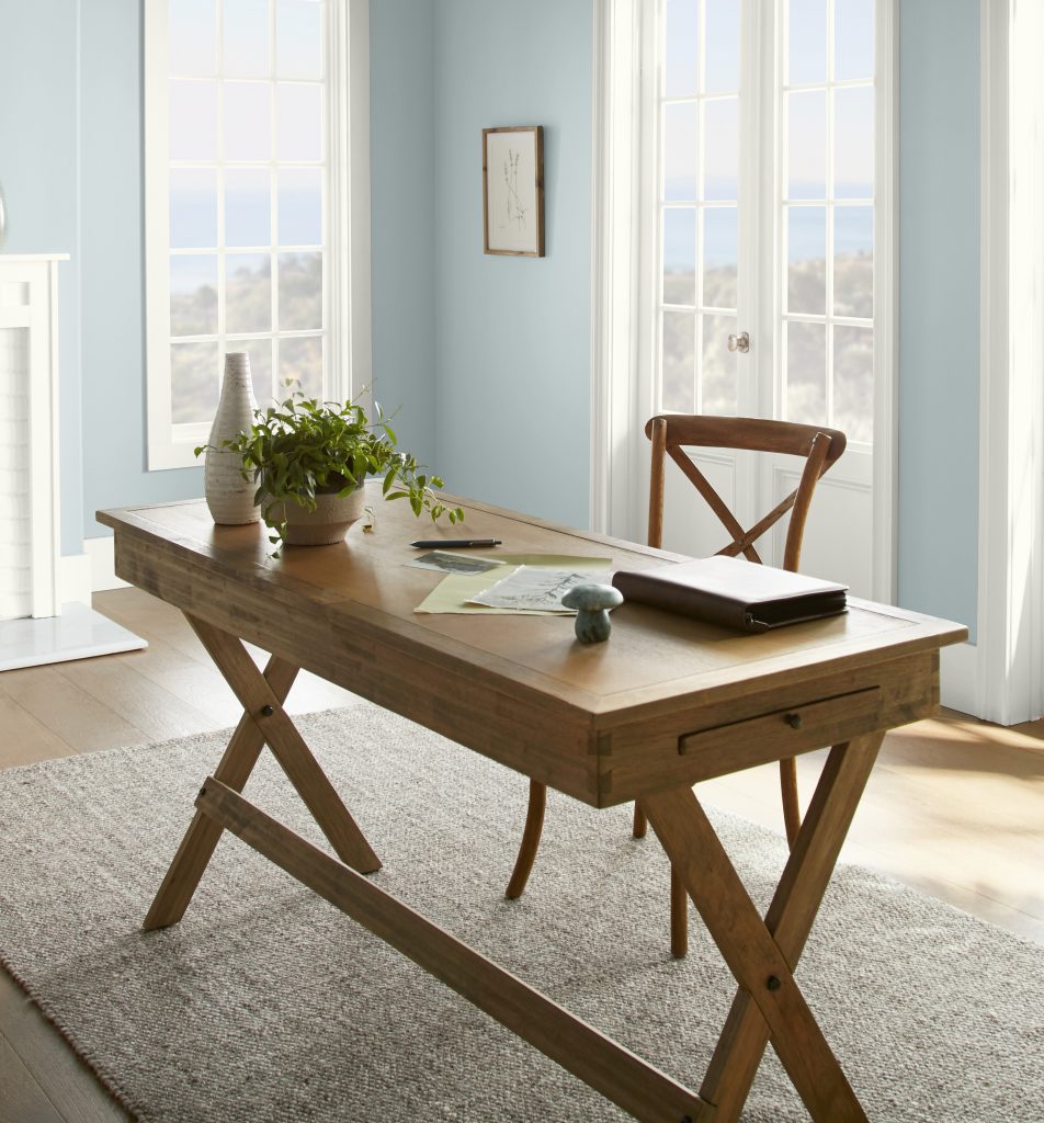 A casual home office with light blue walls. The furniture is a mid-tone wood color. 