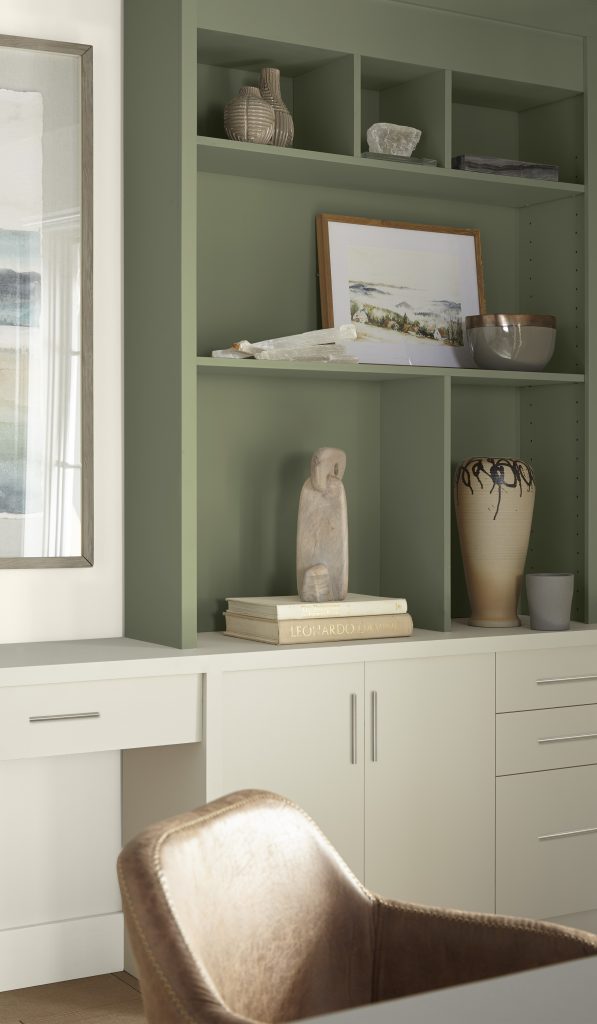 Home office with sage green built-in shelves, white cabinets, and a tan leather chair.