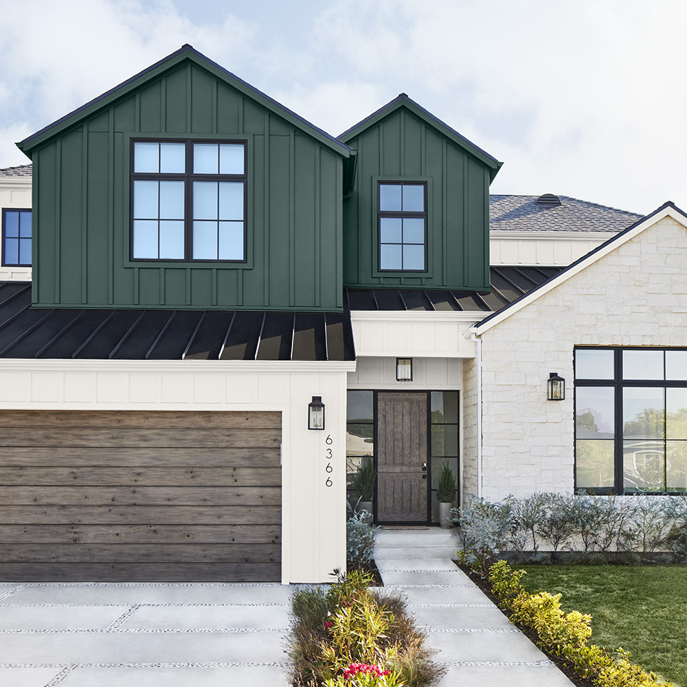 A new built two-story house with dark green and white exterior, wooden garage door, and landscaped front yard.