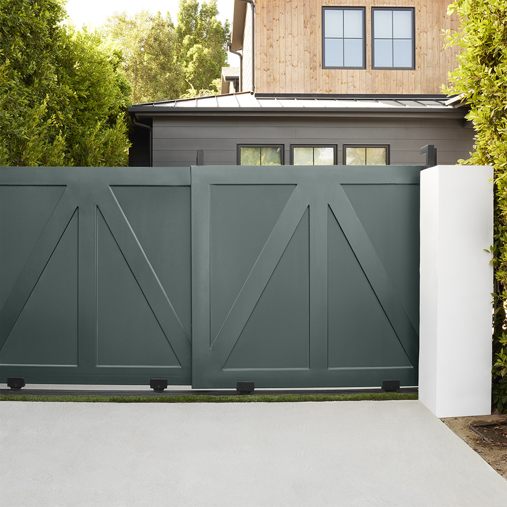 A dark green sliding gate with geometric design, set in front of a two-story home with wood and dark gray exterior.