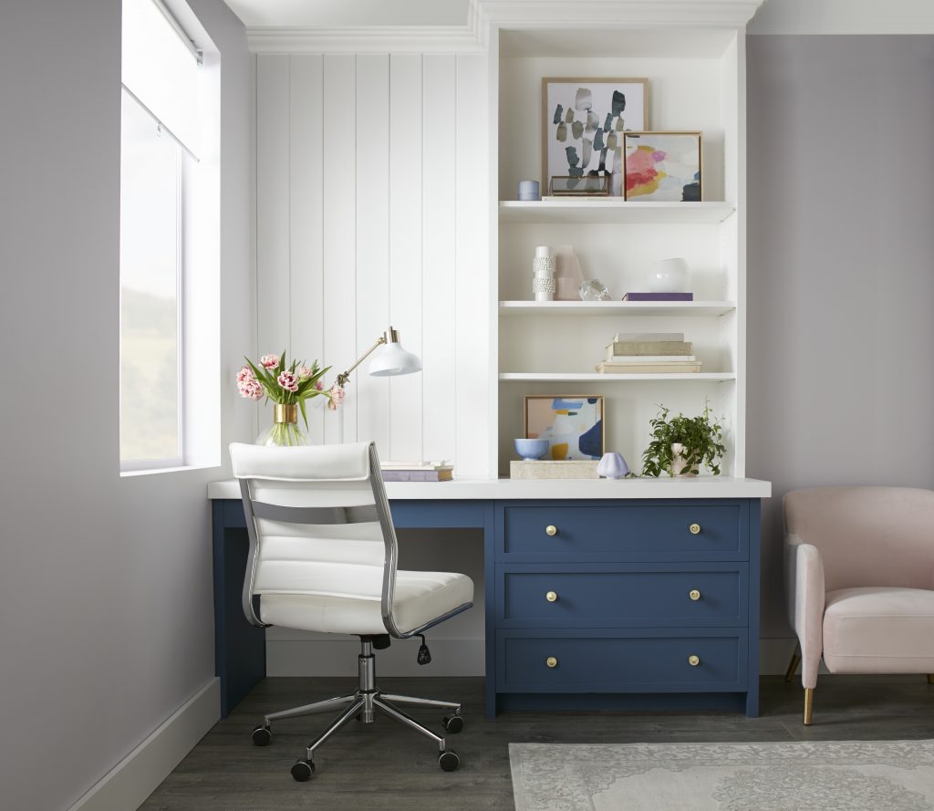 Home office with white walls, navy blue drawers, white desk and chair, and a light purple armchair.