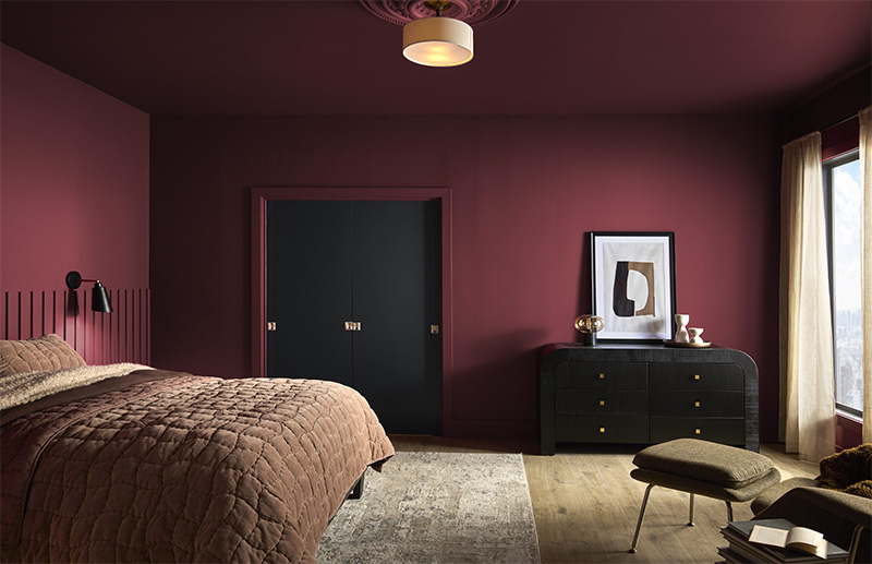 Bedroom with dark red walls, brown bedspread, black dresser, and beige curtains.