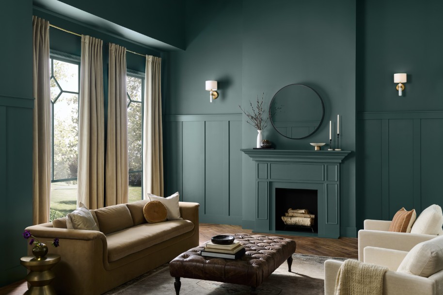 Image shows living room with dark teal walls, tan sofa, fireplace, and natural light from a large window with beige curtains.