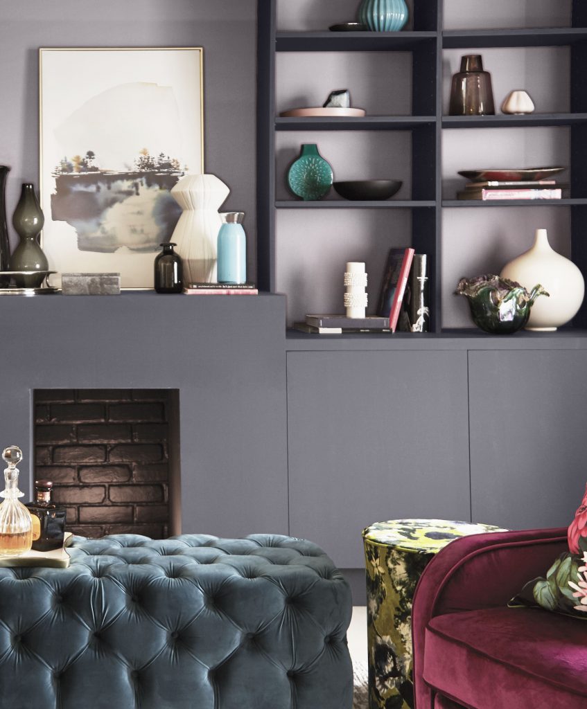 A living room with the fireplace and cabinets in a steely gray hue, while the backdrop of the shelves is in an elegant lavender gray.