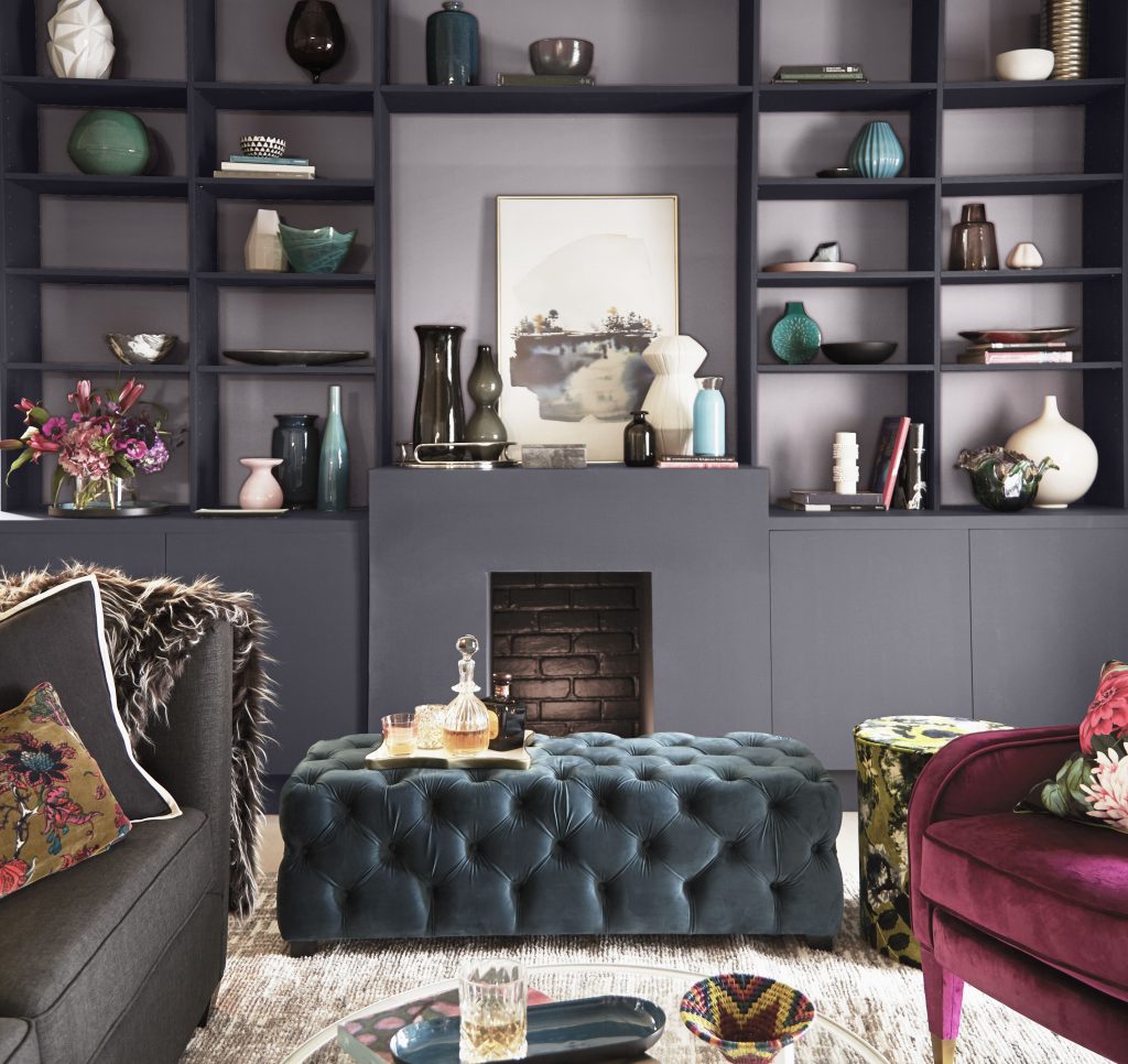 A living room with the fireplace and cabinets in a steely gray hue, while the backdrop of the shelves is in an elegant lavender gray.