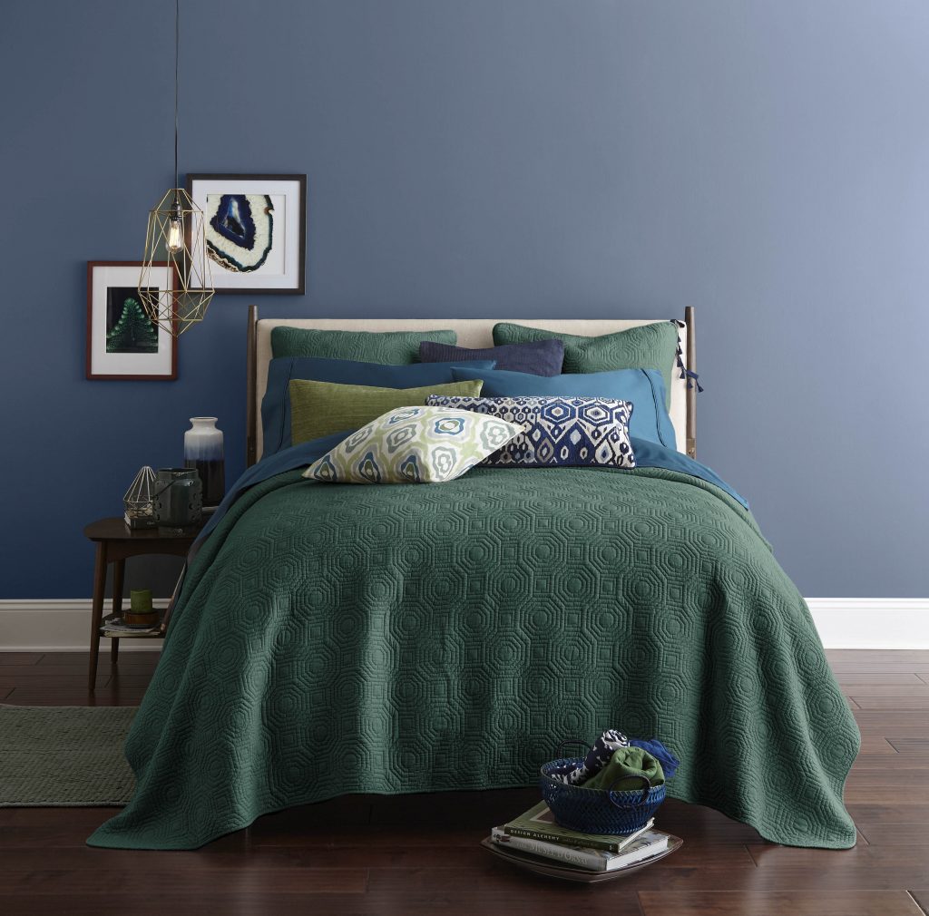 A bedroom with walls painted in a calming blue hue painted on the walls. Bedding is in green, blue and purple jewel tones.