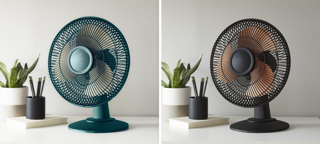 Tabletop fan styled on a desk, shown in rich teal alongside a painted black version for a dramatic color contrast.
