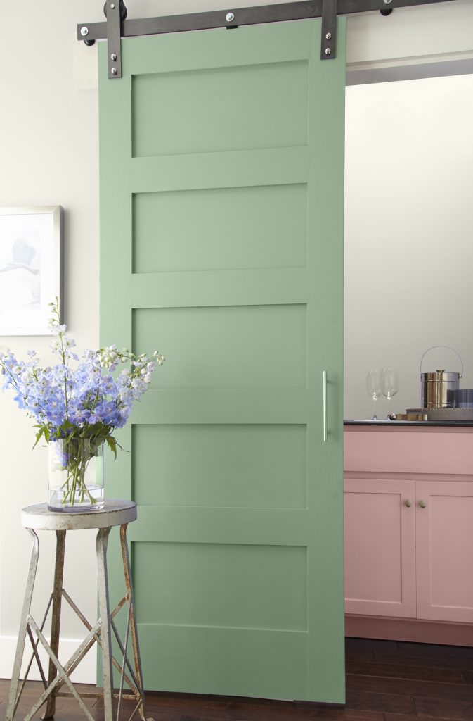 a nook with a door in a pastel green and a dresser peaking out in a pastel pink.