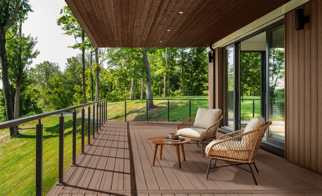 A covered outdoor deck with two different wood stain colors.  Taupe is the wood stain color of the floor and wood ceiling is a color called Chocolate. The deck is furnished with two lounge chairs and a small table, overlooking a grassy landscape with trees.