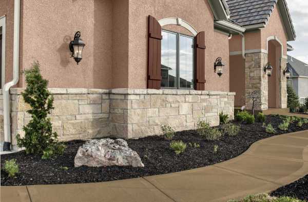 A home exterior with textured stucco painted Iced Copper, accented by Blank Canvas trim and Dark Cherry Cola shutters, featuring stone, arched windows, and a curved walkway bordered by fresh landscaping.