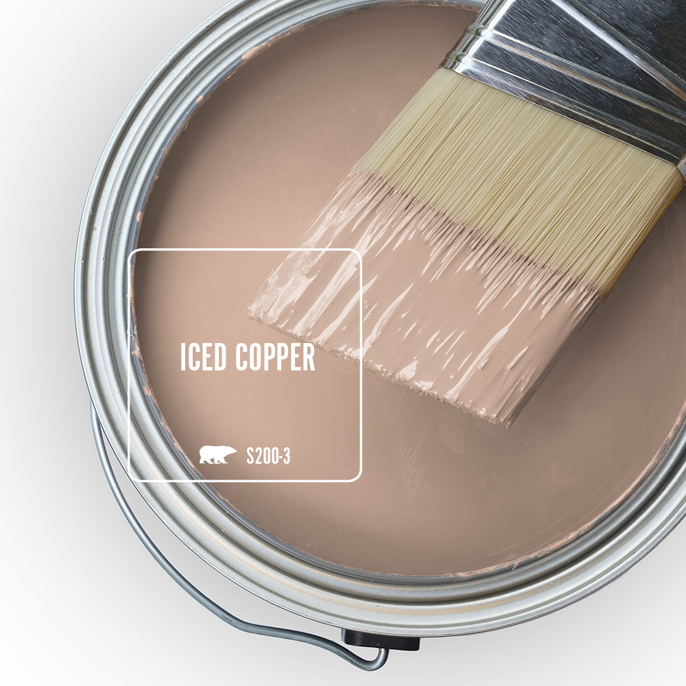 An open paint can filled with warm color called Iced Copper, with a paintbrush resting across the rim and dipped into a smooth warm color, highlighting the labeled shade Iced Copper S201-3.