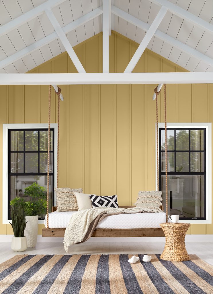 A natural wood swing hangs against a warm golden home with light trim.