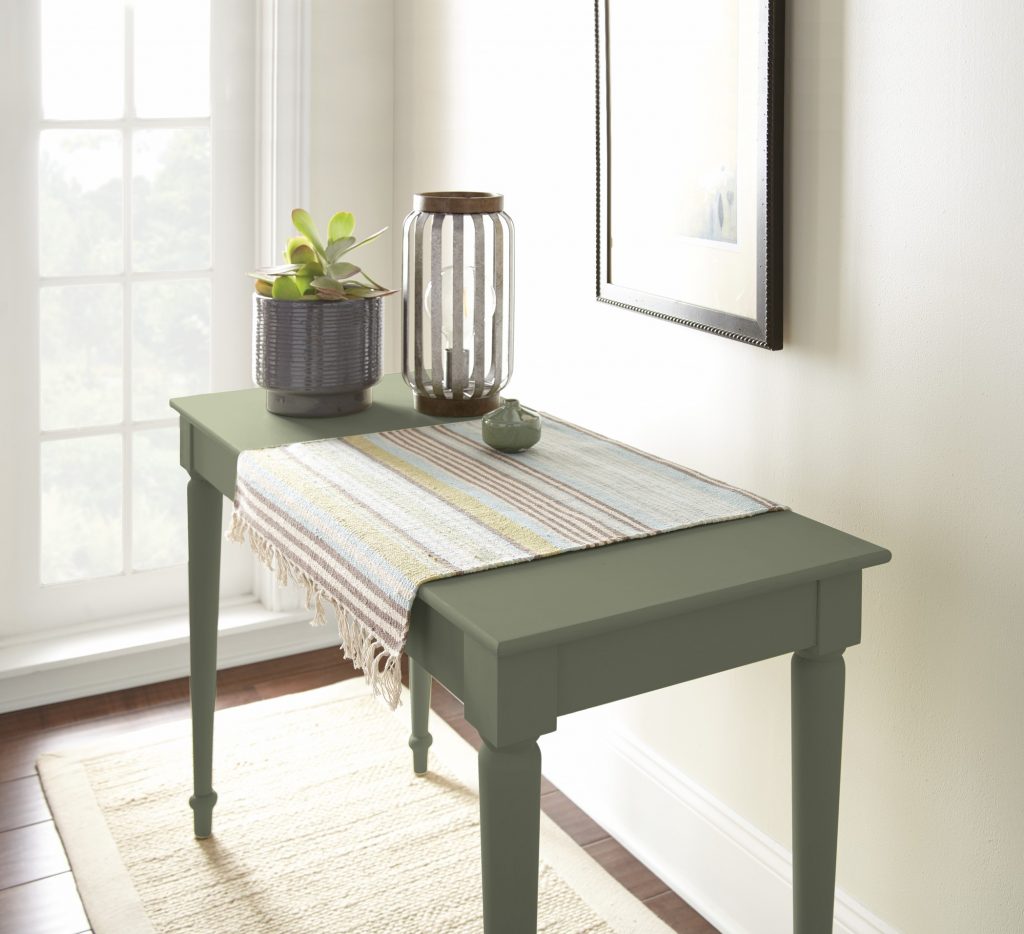 A console table painted in “Ecological,” styled with a plant, decorative accents, and a woven runner in a light-filled hallway.