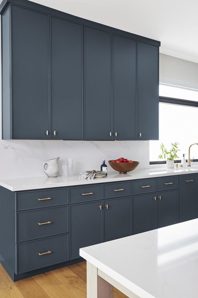 Kitchen with blue grey cabinets, warm gold accents, and white countertops.