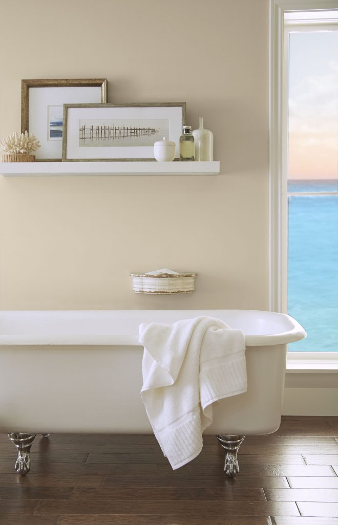 Bathroom with warm neutral walls and a freestanding tub beside a window.
