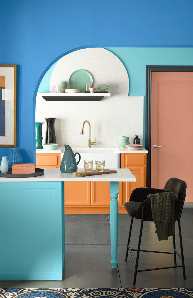 Colorful kitchen nook with orange cabinets, blue walls, and a terracotta-colored door.
