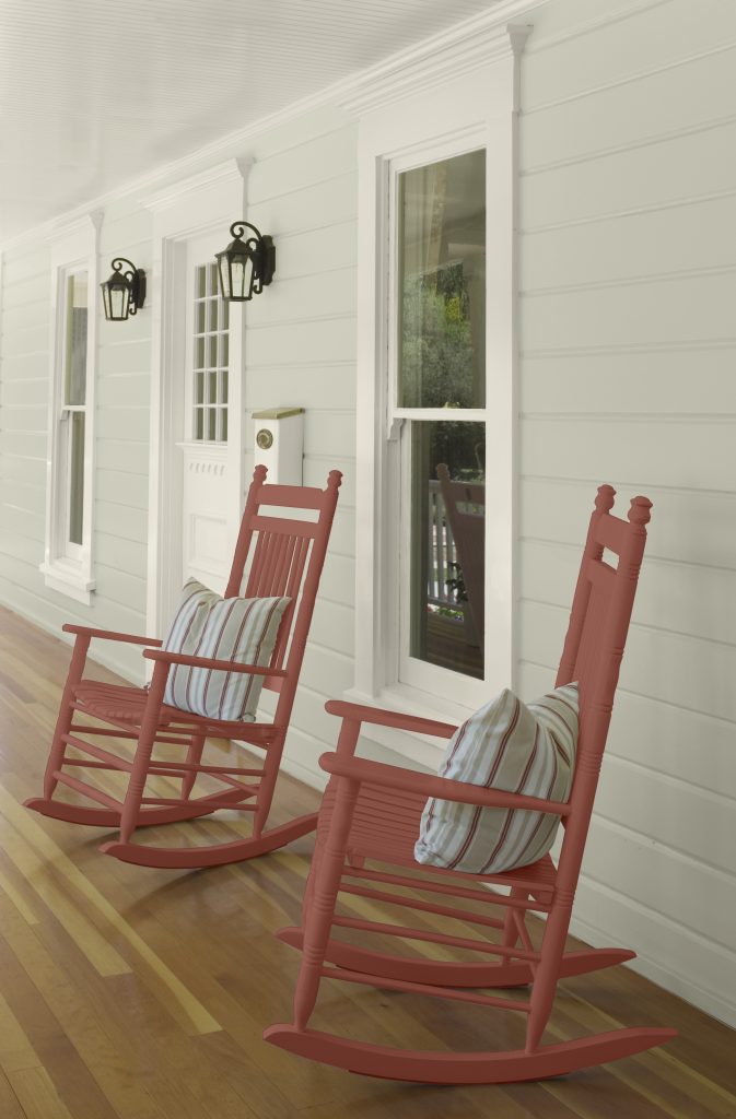 Two warm-toned rocking chairs sit on a porch with soft green siding.