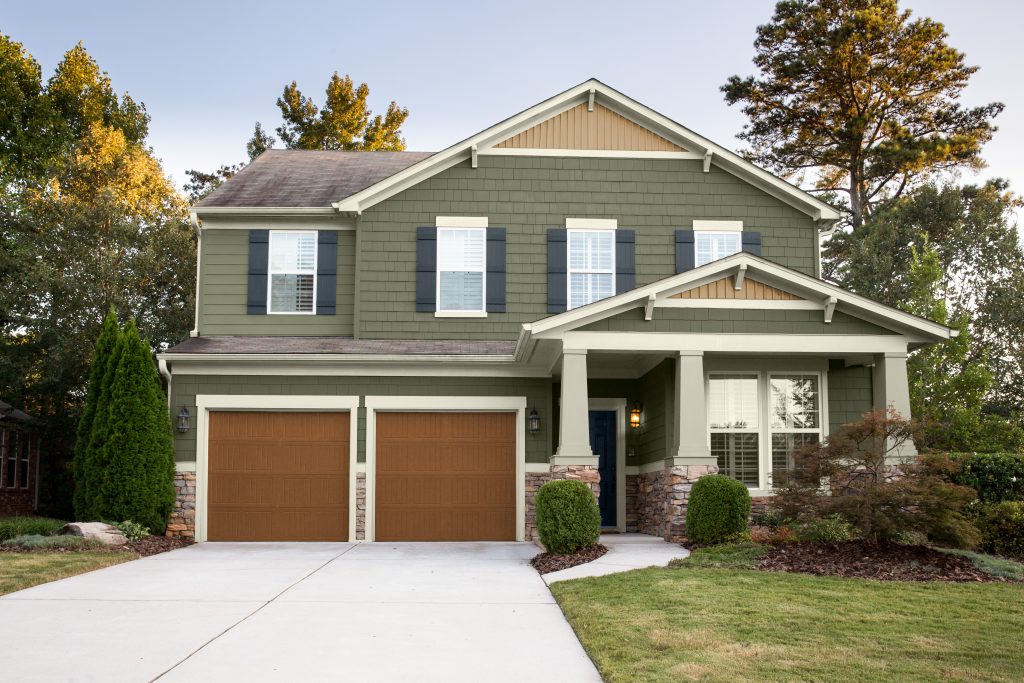 A two-story mostly green color Craftsman-style home with a double garage, covered front porch, and landscaped yard.
