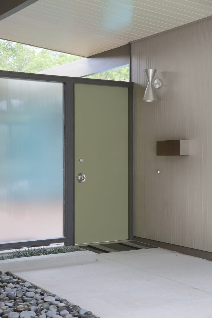 A Mid-century modern entryway with a green front door, frosted glass panels, brown siding, and concrete walkway.