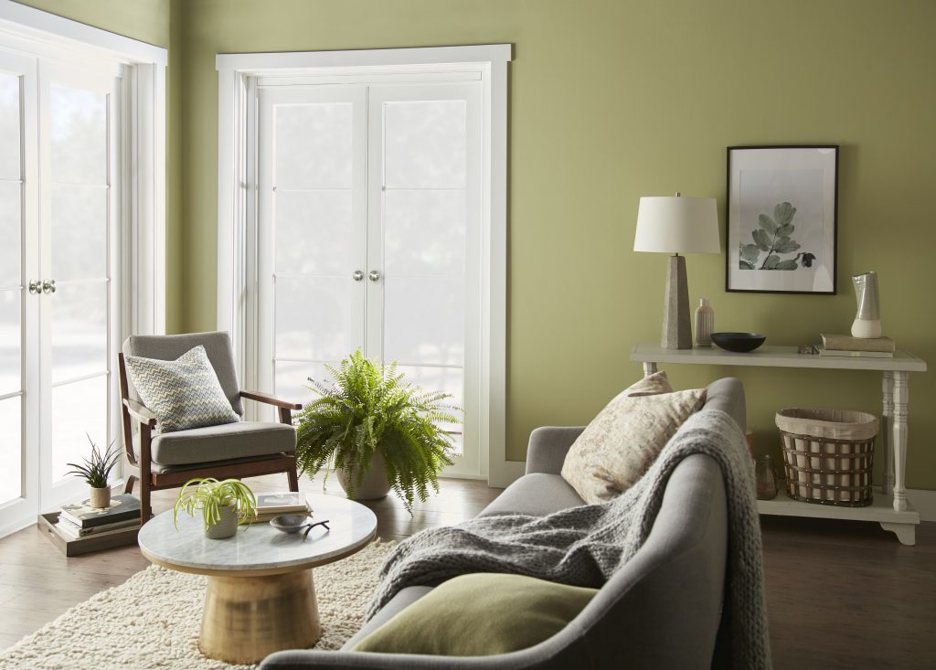 Living room with Fresh Artichoke green wall paint, natural wood furniture, soft neutral upholstery, indoor plants, and layered textures for a restorative earthy color palette.