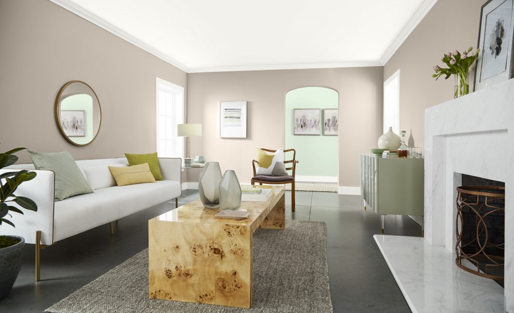 A living room with walls painted in Wheat Bread, featuring a white sofa, natural wood coffee table, gray area rug, fireplace and soft green décor.
