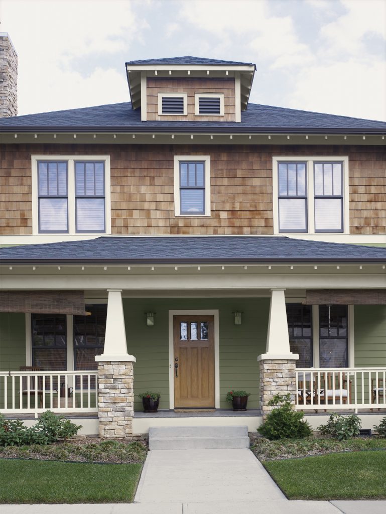 A craftsman-style home with a covered front porch, wood front door, stone columns, and shingle siding.