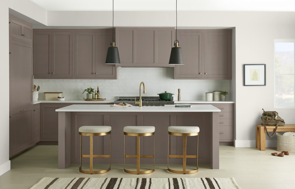 An elegant taupe-brown kitchen featuring floor-to-ceiling cabinetry, a matching island, white countertops, brass accents, and black pendant lights. The layered neutral tones create a refined and sophisticated atmosphere.