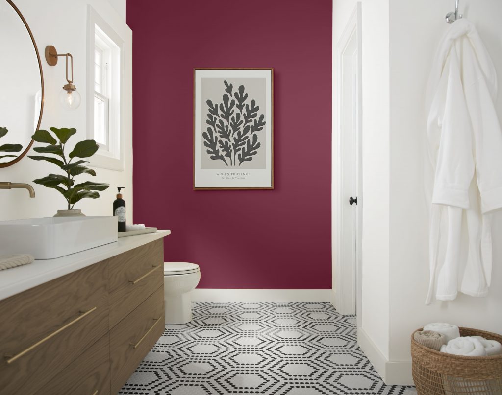 Bathroom with Sugar Beet berry-toned accent wall, white trim, wood vanity, patterned floor tile, and soft spa-like styling.