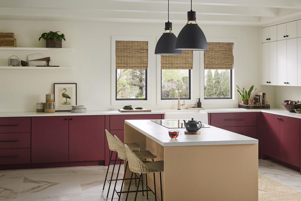 This kitchen showcases confident deep red paint color on the lower cabinets paired with a tan brown island, natural textures, and modern black lighting.