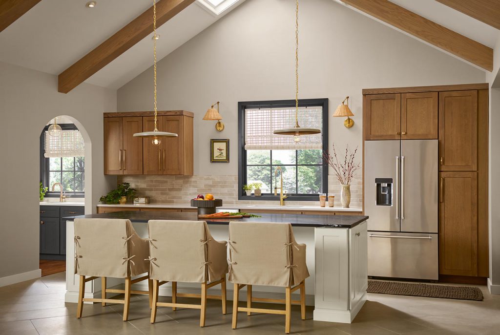 A neutral greige kitchen with layered warm wood cabinets, creamy island cabinetry, beige backsplash tile, brass lighting, and dark charcoal gray accents. The mix of warm greige walls, natural wood tones, and almost-black trim adds depth, making the neutral palette feel balanced, textured, and dimensional.