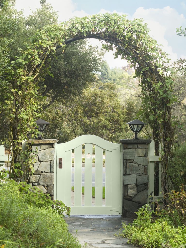 Exterior garden gate painted in a pale cabbage-inspired green, surrounded by stone, greenery, and natural landscaping for an indoor-outdoor color palette connection.