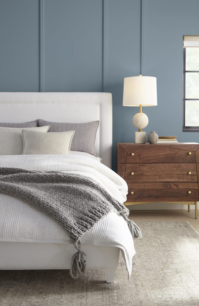 Bedroom with muted blue walls painted in Adirondack Blue, white bedding, and warm wood nightstand.