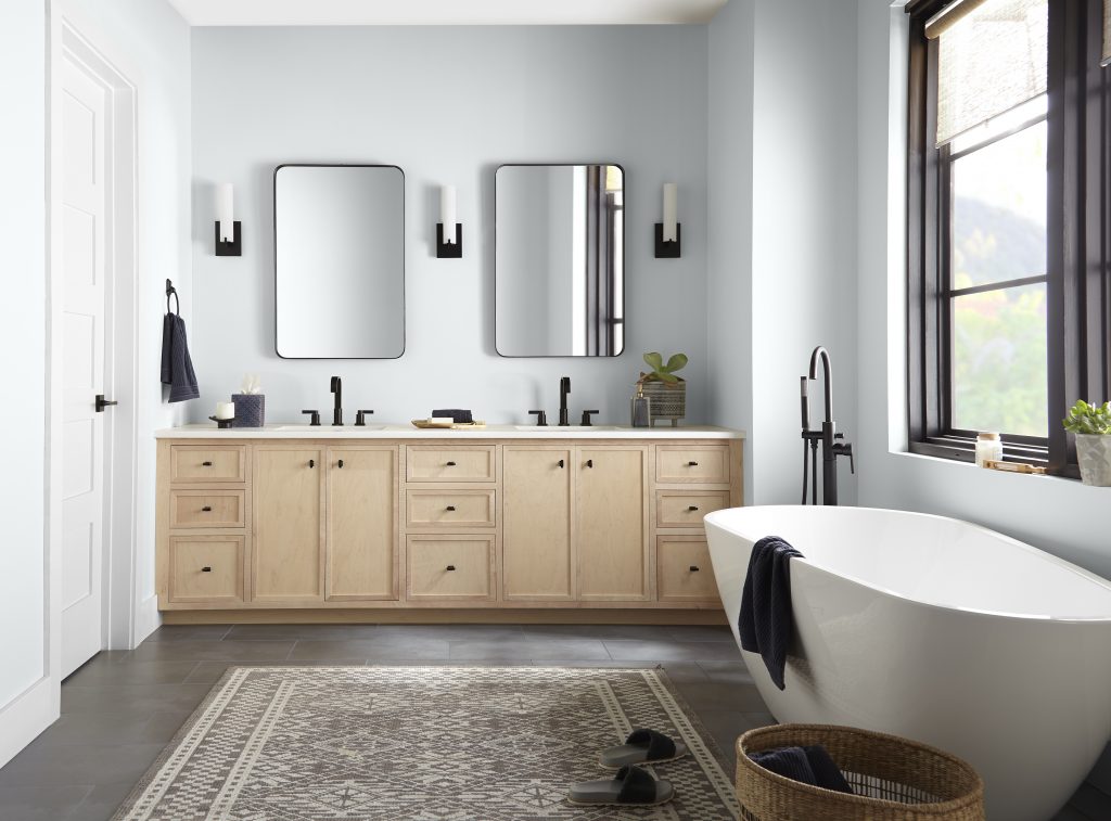 Bathroom with soft blue-gray walls in Etched Glass, light wood vanity, and freestanding tub.