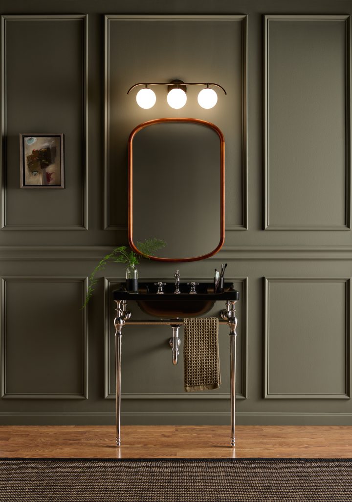 A sophisticated small bathroom with decorative molding painted in BEHR Grounded, featuring a black console sink, rounded mirror, globe vanity lights, and warm wood flooring.