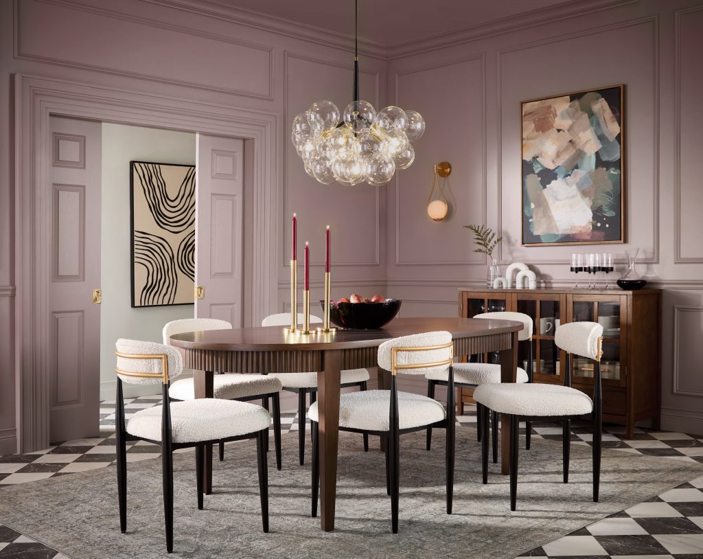 An elegant dining room with soft mauve walls, decorative wall molding, an oval dining table, upholstered chairs, a statement glass chandelier, black-and-white checkered floor, and layered artwork.