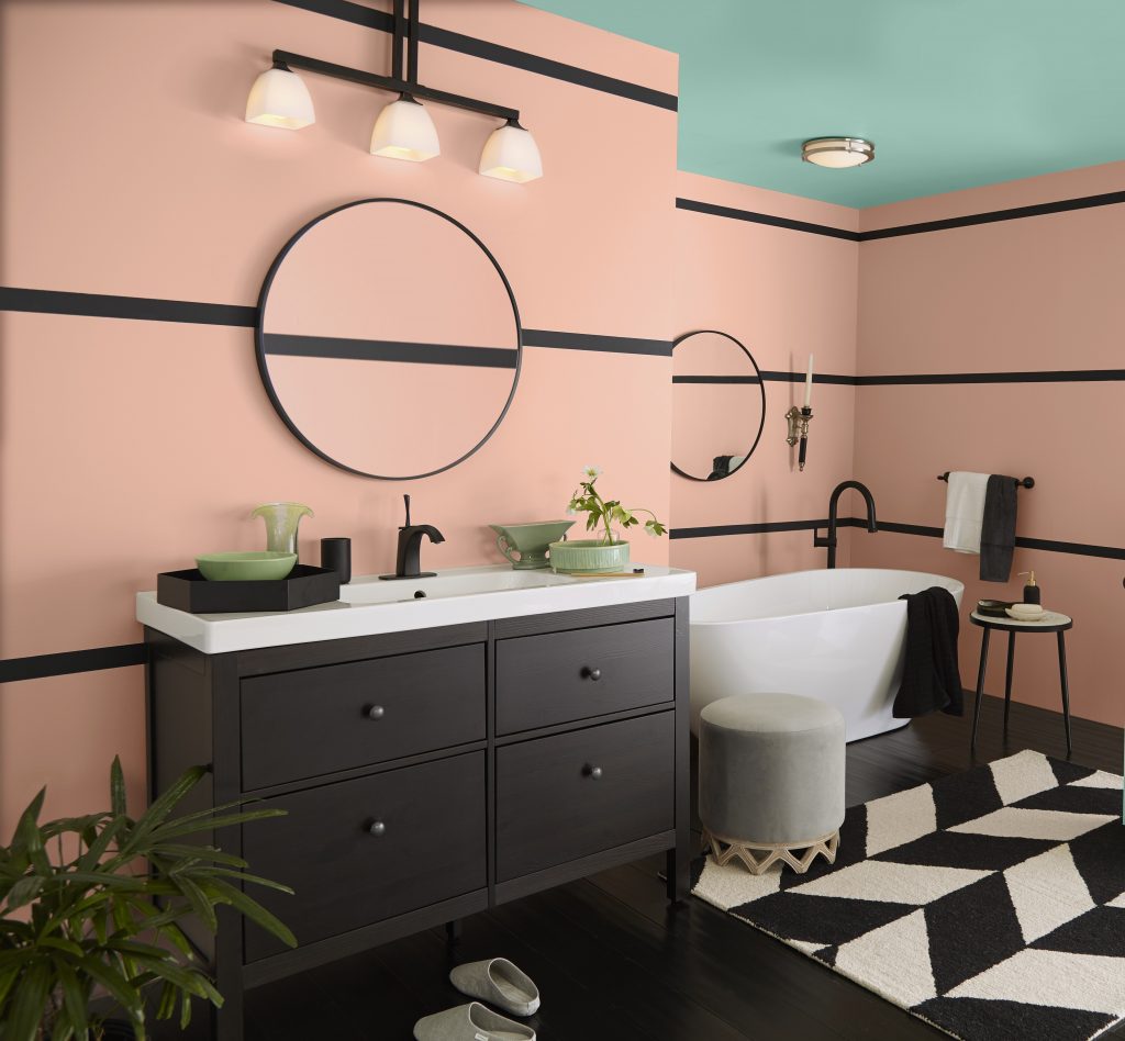An Art Deco-inspired bathroom with peach walls, teal ceiling and door, black trim, dark vanity, round mirrors, freestanding tub, and bold black-and-white geometric floor tile.