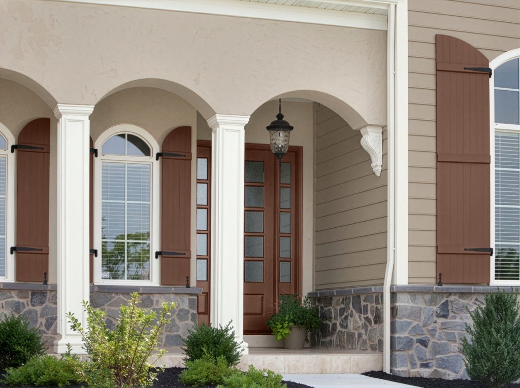 A close-up of a traditional home exterior featuring warm taupe siding, darker taupe shutters, white trim, arches and columns, stone accents, and a dark wood front door.