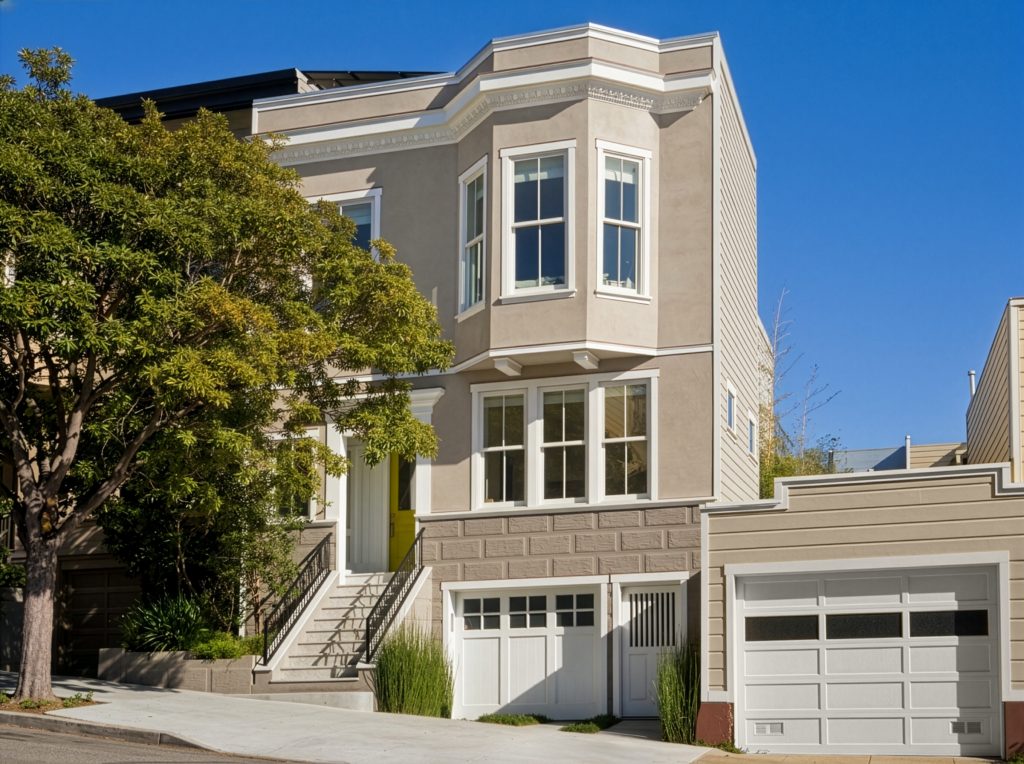 A narrow multi-story townhome with a neutral taupe paint color called Wheat Bread, white trim and windows, a bright green front door, and an integrated garage.